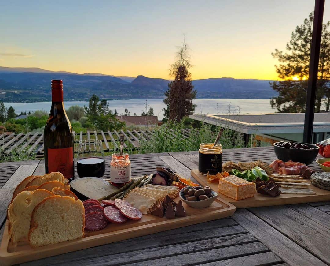 Charcuterie board with a bottle of wine on a table overlooking a vineyard and Lake Okanagan at a Naramata Bench winery.